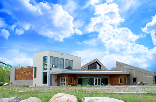 The Helen Schuler Nature Centre building with green grass and blue skies with white fluffy clouds in the background.